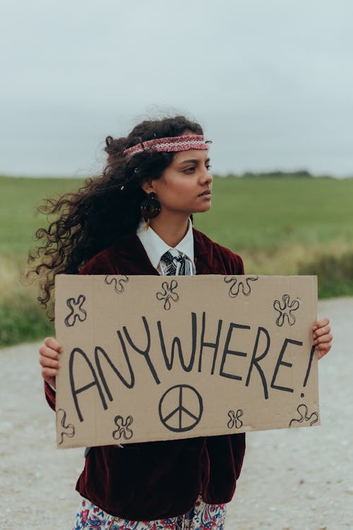 Young Hippie Woman with a Hitchhiking Sign Saying "Anywhere"