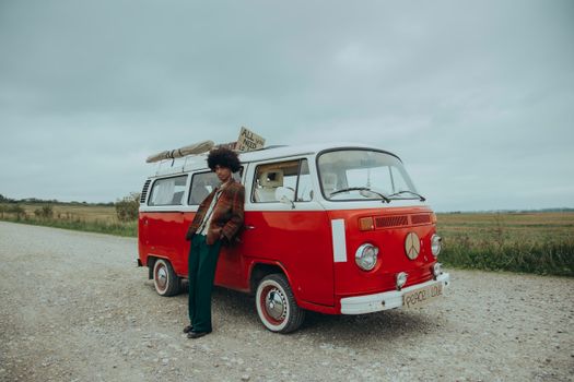 Stylish man leans on a retro van in a scenic countryside setting, exuding 60s hippie vibes.