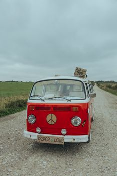 A vintage red van with peace signs and love messages on a rural dirt road, promoting harmony.