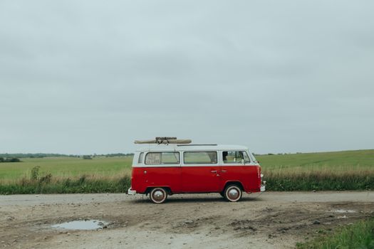 A classic red vintage van parked on a rural unpaved road, evoking a sense of nostalgia and wanderlust.