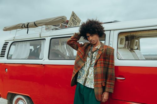 Free Man with afro in retro attire leaning on a vintage red van, embodying 60s hippie vibes. Stock Photo