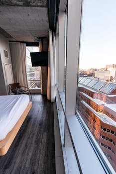 Stylish apartment bedroom with panoramic Boston skyline view through glass windows.
