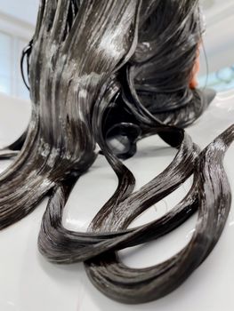 Close-up of brunette woman's wet hair receiving treatment at a salon.