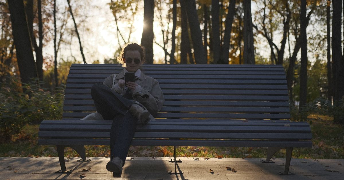 Person sitting on a park bench looking at a sunset without a phone in hand