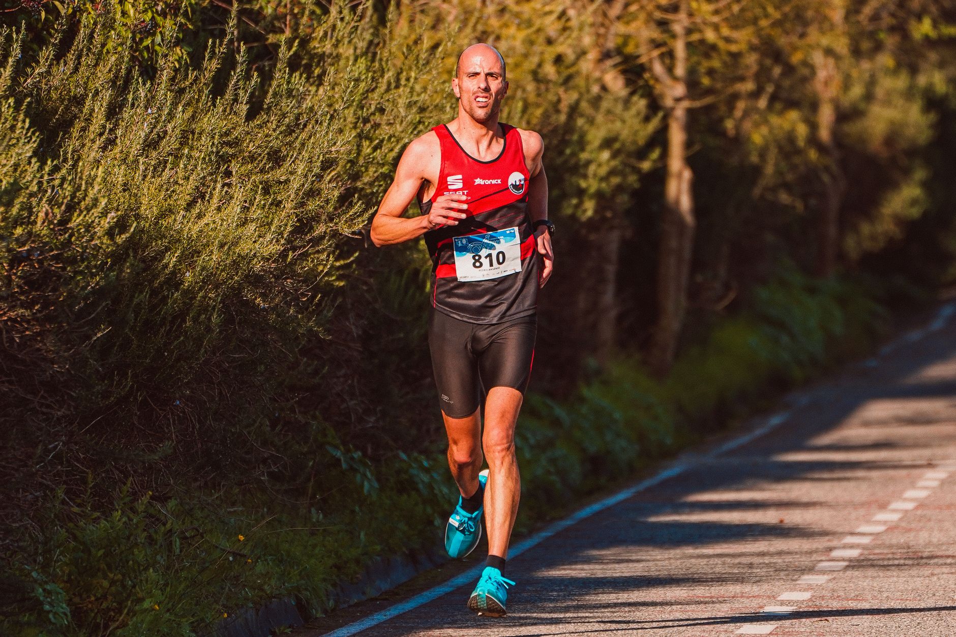 Athlete running a marathon on a sunny day along a scenic, wooded road