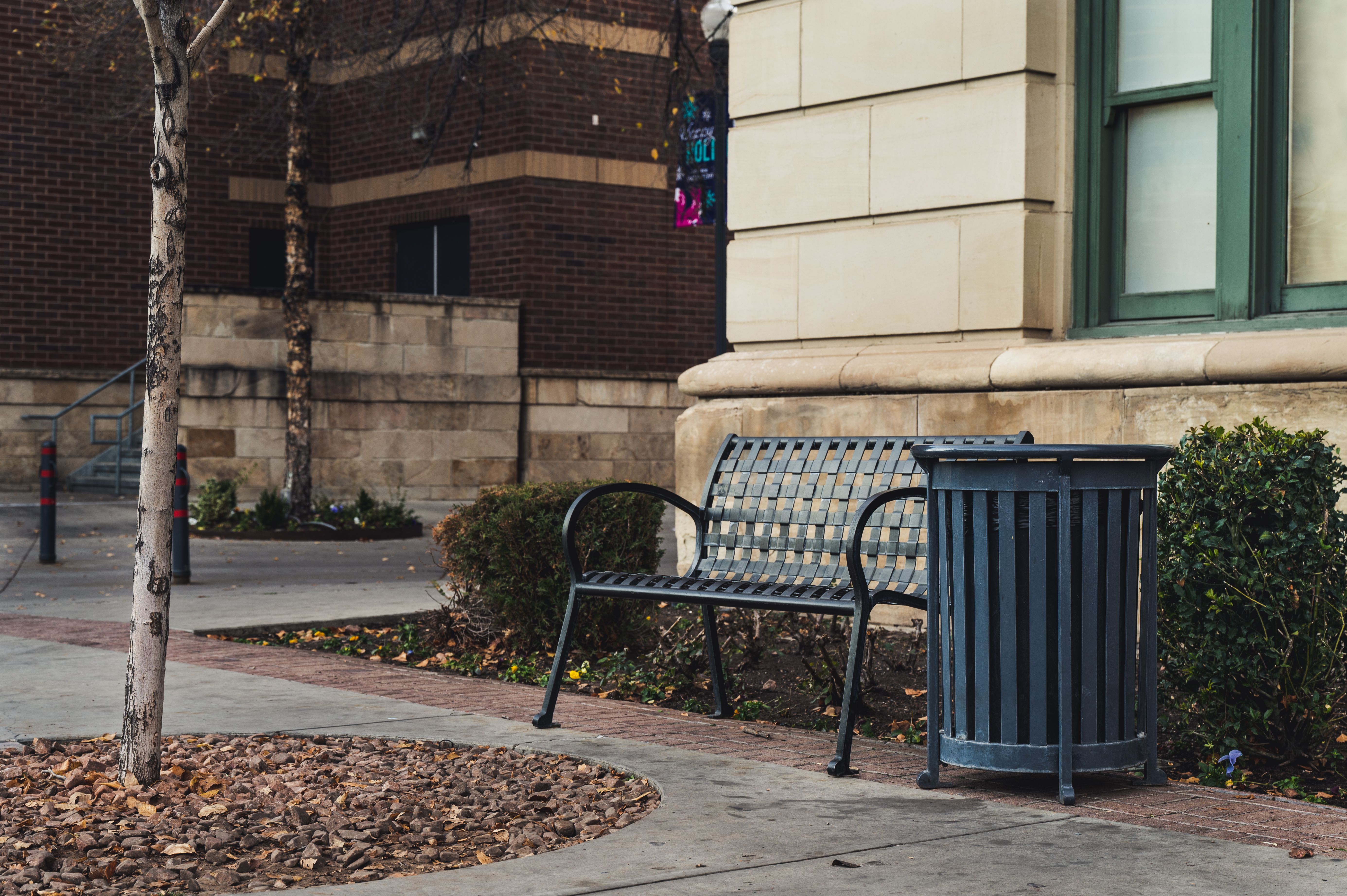 Street view showing an empty park bench beside a trash bin in an urban area.