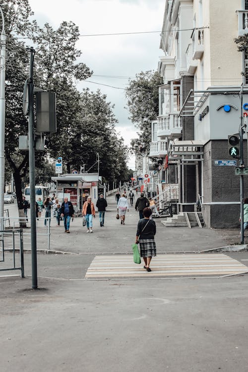Photo of People Walking on Sidewalk and a Woman Crossing a Pedestrian Lane