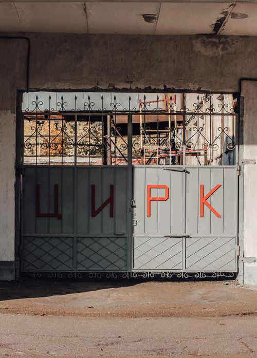Free A rustic iron gate featuring Cyrillic letters in a sunlit urban setting. Stock Photo