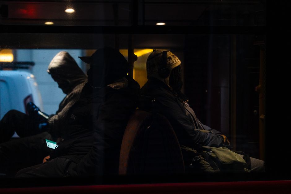 Silhouetted passengers seated inside a bus at night, captured in an urban UK setting.