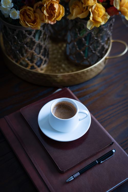 Free A cozy scene featuring a coffee cup on a planner with vibrant flowers, perfect for a relaxing ambiance. Stock Photo