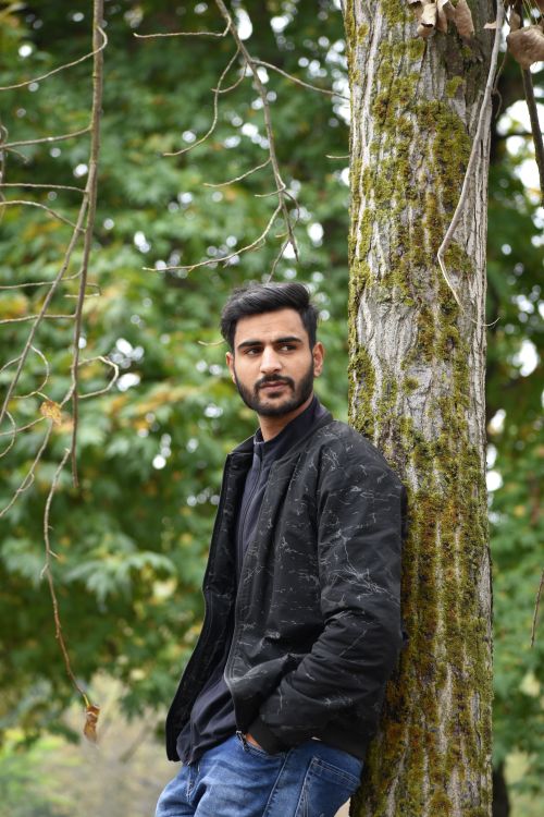 Free A thoughtful man in a black jacket leans against a moss-covered tree, surrounded by lush greenery. Stock Photo
