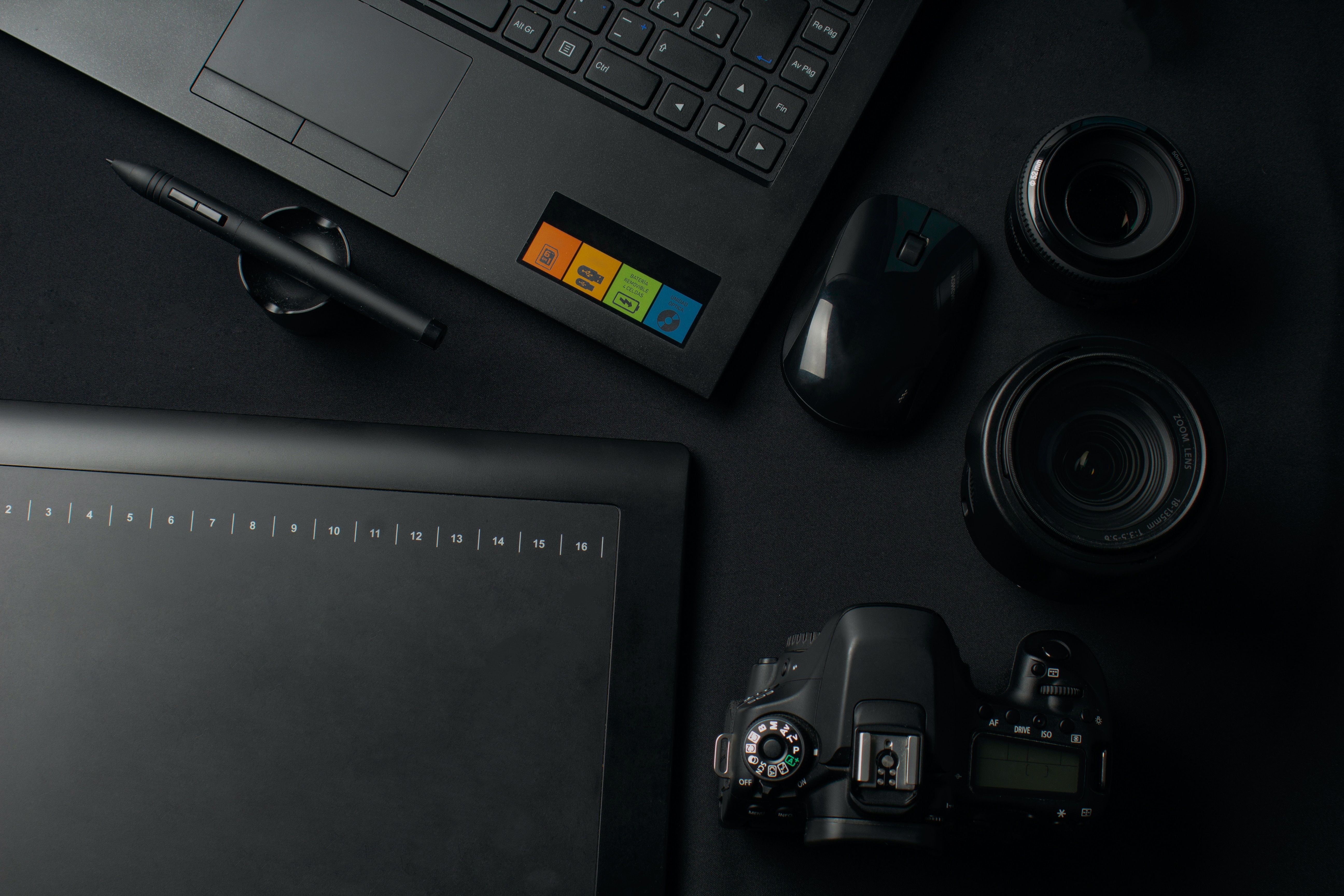 Top view of a modern workspace setup featuring a camera, laptop, graphic tablet, and lenses for photography and editing.