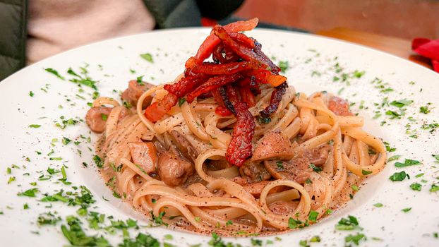 Close-up of a savory pasta dish featuring bacon and herbs on a white plate.