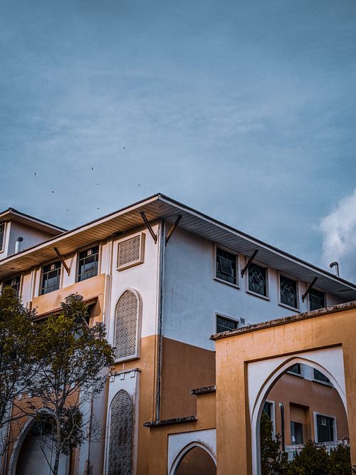 Free Low-angle view of a modern building's exterior design under a blue sky, showcasing concrete structures. Stock Photo