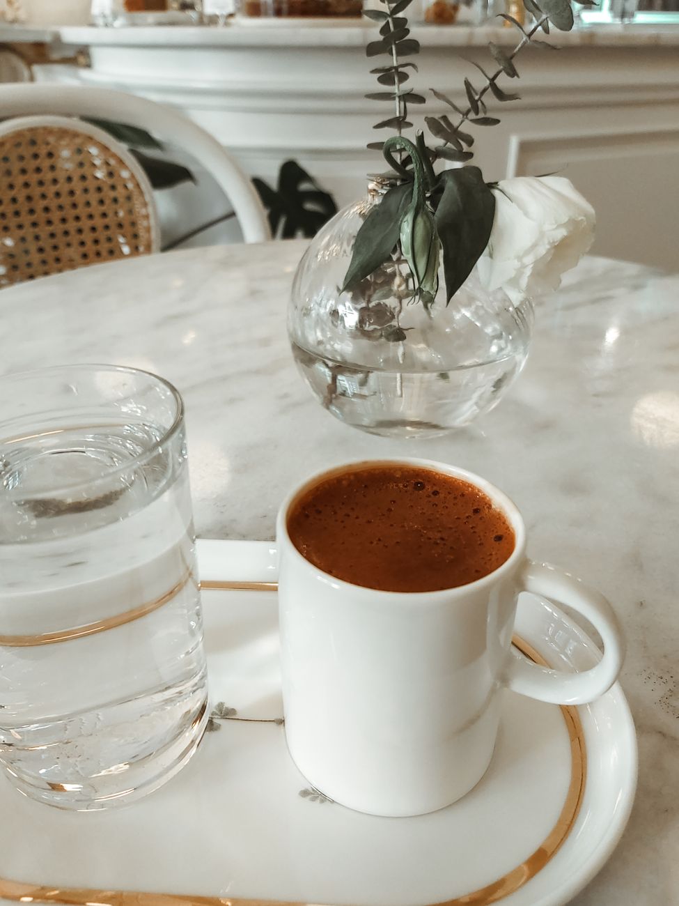 A chic coffee setup featuring an espresso cup and glass of water on a marble table with decorative vase.