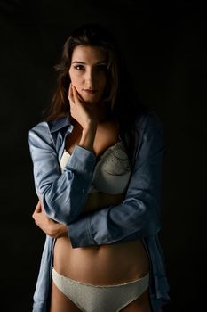 Artistic portrait of a woman wearing lingerie and a blue shirt on a dark background.