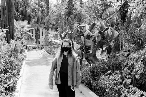 A Grayscale Photo of Woman Wearing Face Mask while Standing Between Plants