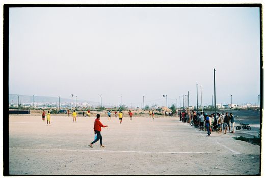 Amateur football match in an open field in Morocco with local players and watchers.