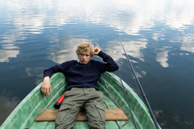 Teenager Resting In Green Boat Floating On Calm Waters