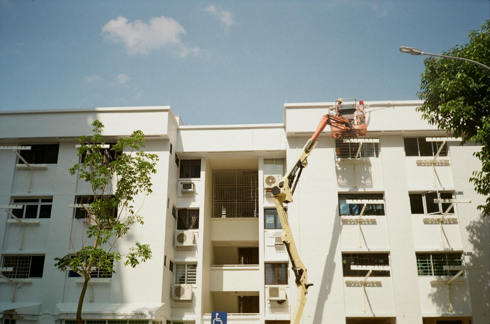 An exterior view of a residential building with maintenance work using a crane lift under clear blue skies.