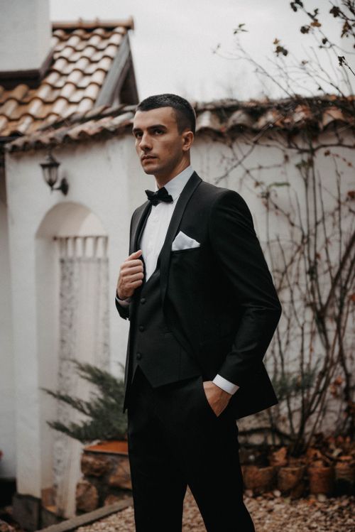 Free Stylish man in a black suit and bow tie, posing outdoors with hand in pocket. Stock Photo