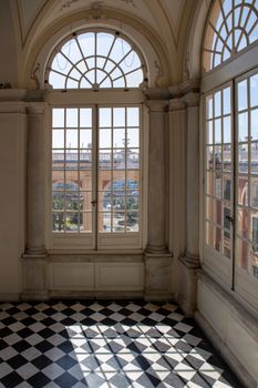 Elegant arched windows in a historic room with a checkered floor. Bright light streaming in creates a contrast.