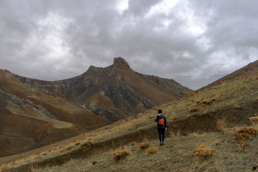 A lone hiker in Van, Türkiye, trekking through rugged mountains under an overcast sky.