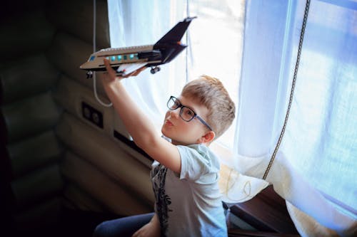 A Boy Sitting Beside a Window Playing with a Toy Airplane