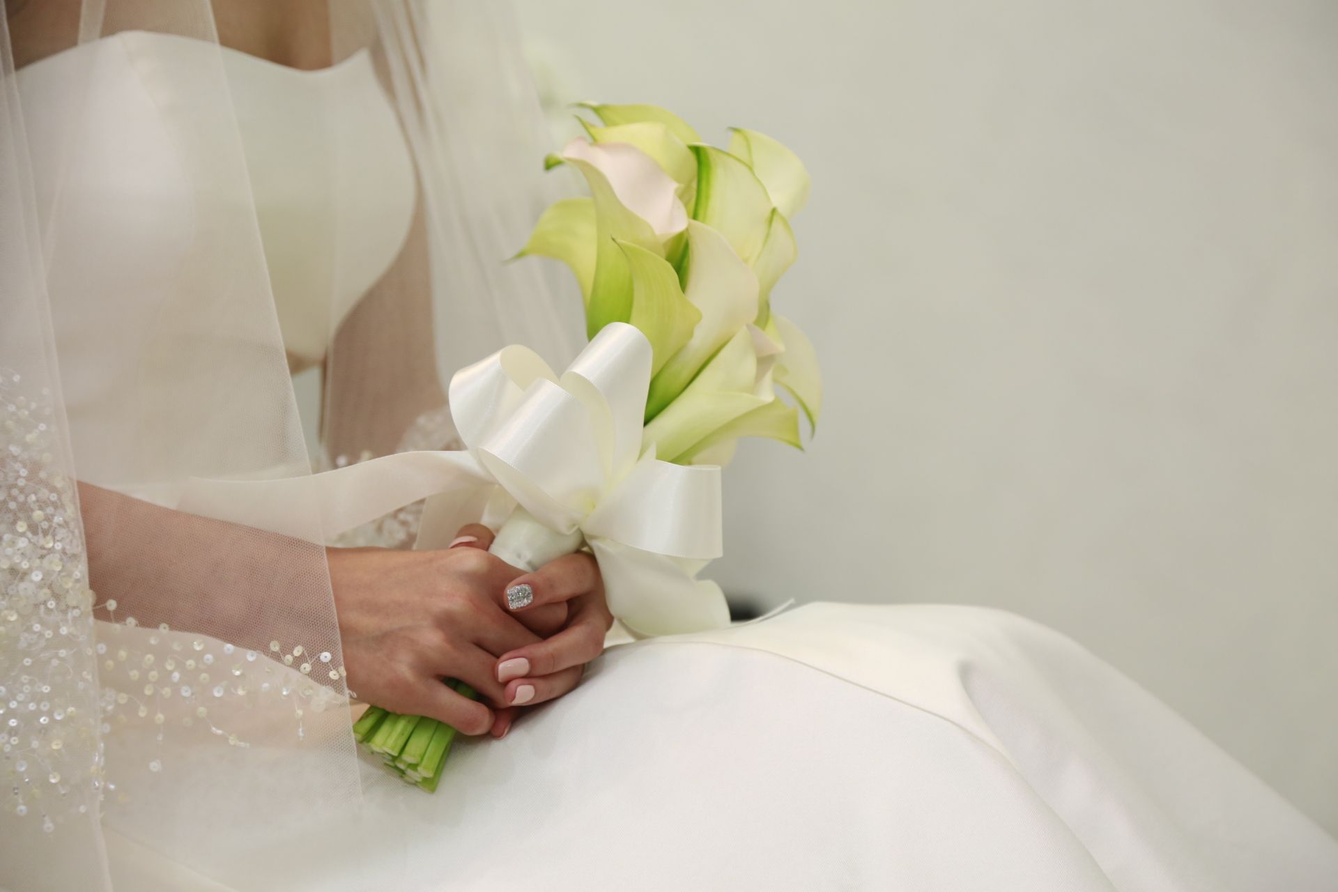 Close-up of a bride holding a bouquet of white calla lilies tied with a satin ribbon.