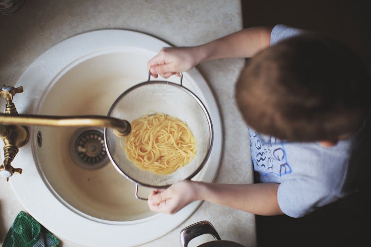 Child Holding A Strainer With Pasta