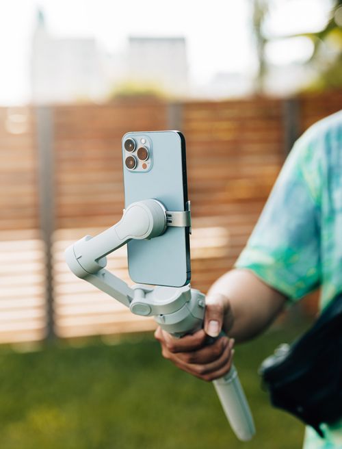 Free Close-up of a smartphone on a gimbal, held by a person outdoors with blurred background. Stock Photo