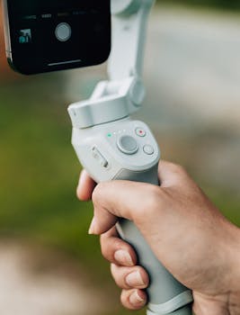A close-up view of a hand holding a smartphone stabilizer outdoors, ideal for filming.