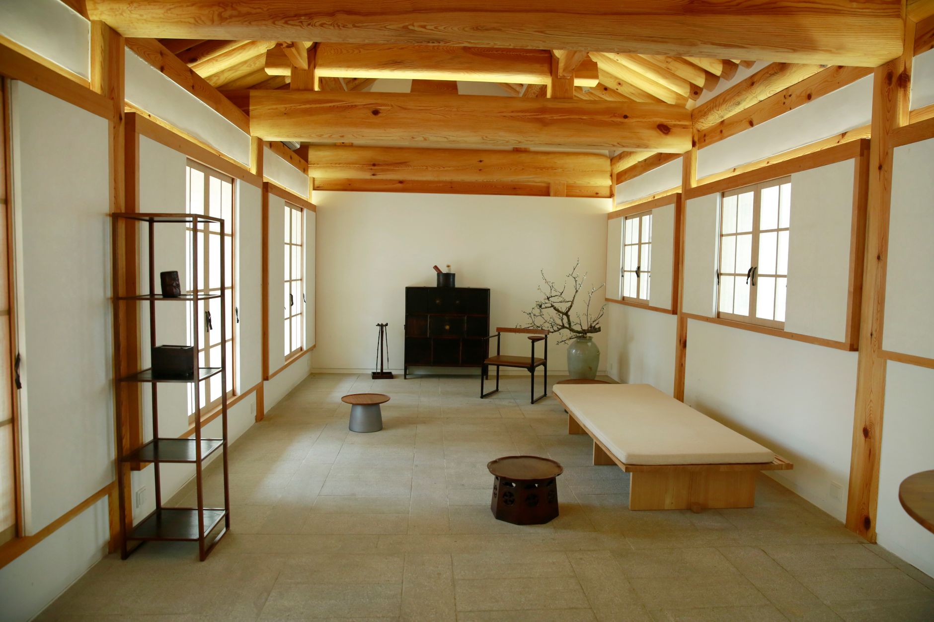 A minimalist room featuring wooden beams, shelves, and traditional seating.