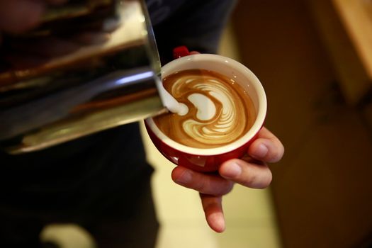 Close-up of detailed latte art pour, with milk swirling into a red coffee cup.