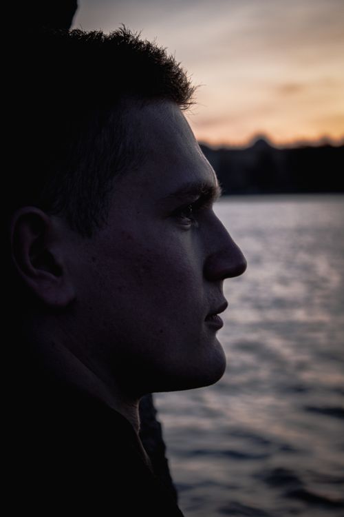 Free Silhouette of a man in profile view gazing at a serene water backdrop during sunset. Stock Photo