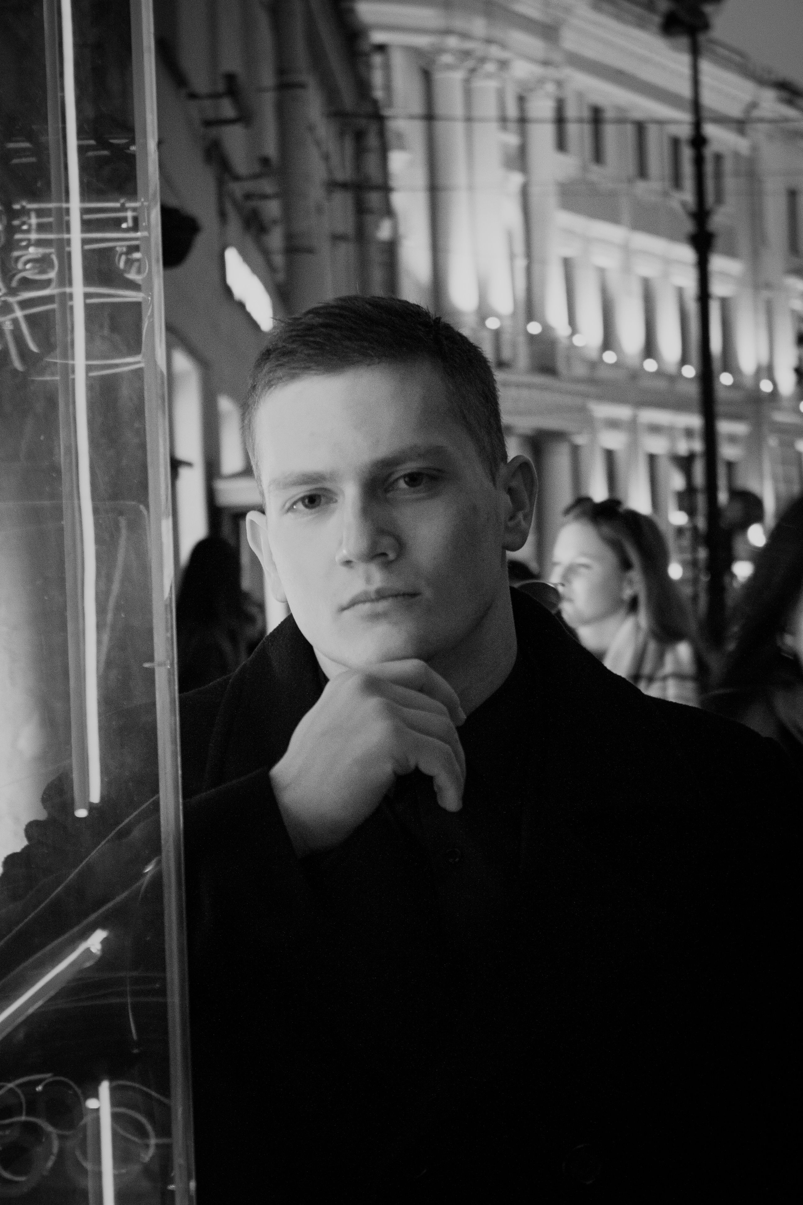Moody grayscale portrait of a man posing on a bustling city street at night.