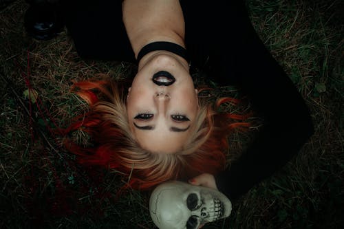 Free A Woman with Dyed Hair Holding a Skull while Lying on Grass Stock Photo