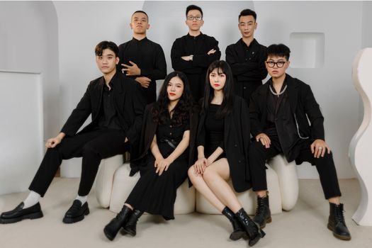A stylish group of young adults posing confidently in black attire in an indoor studio setting.
