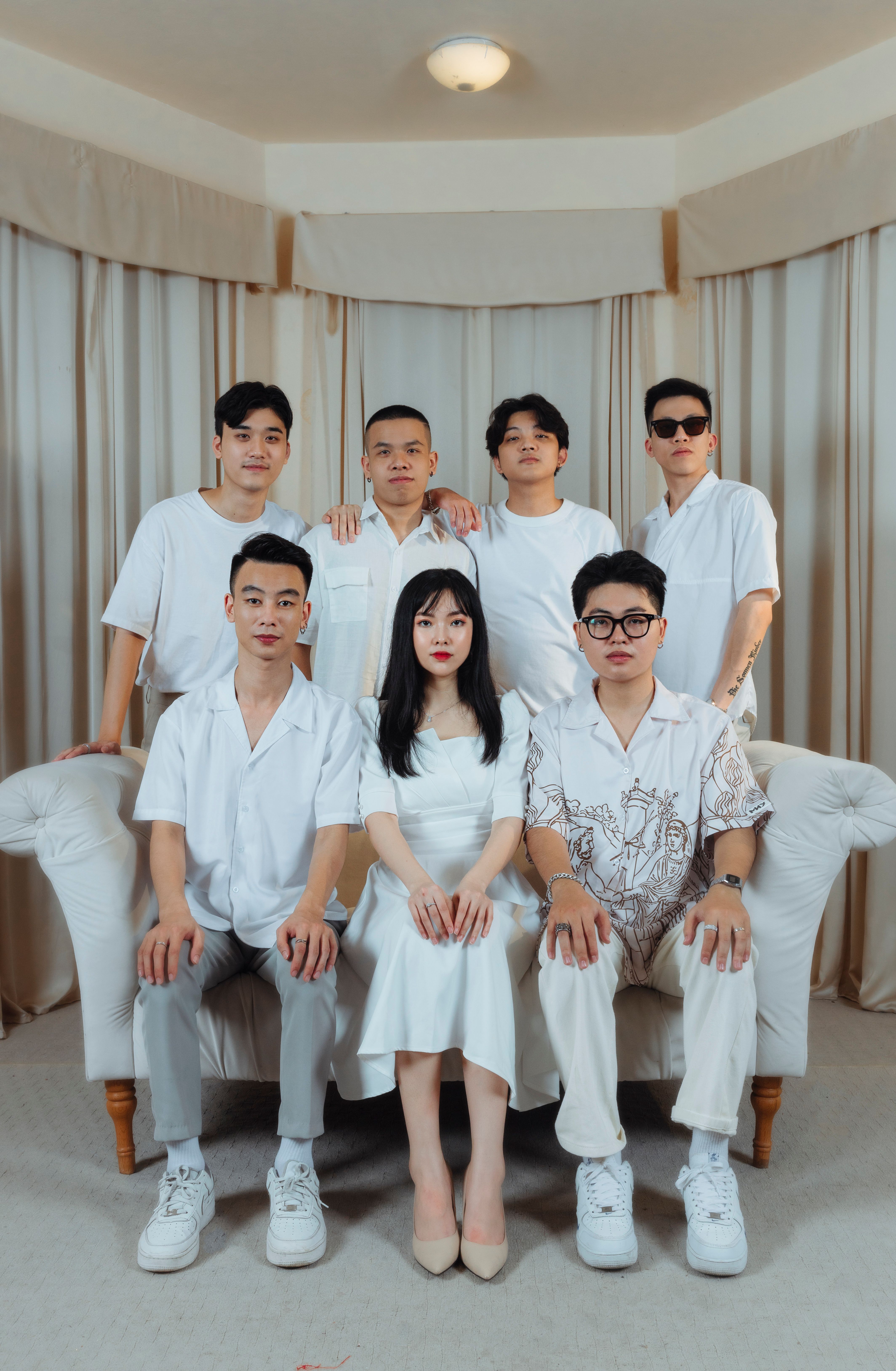 Seven adults in white clothing posing indoors for a group portrait with a modern style.