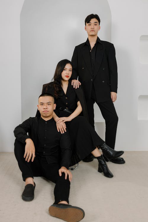 A Young Woman in Black Dress Sitting Between Young  Men in Black Suit