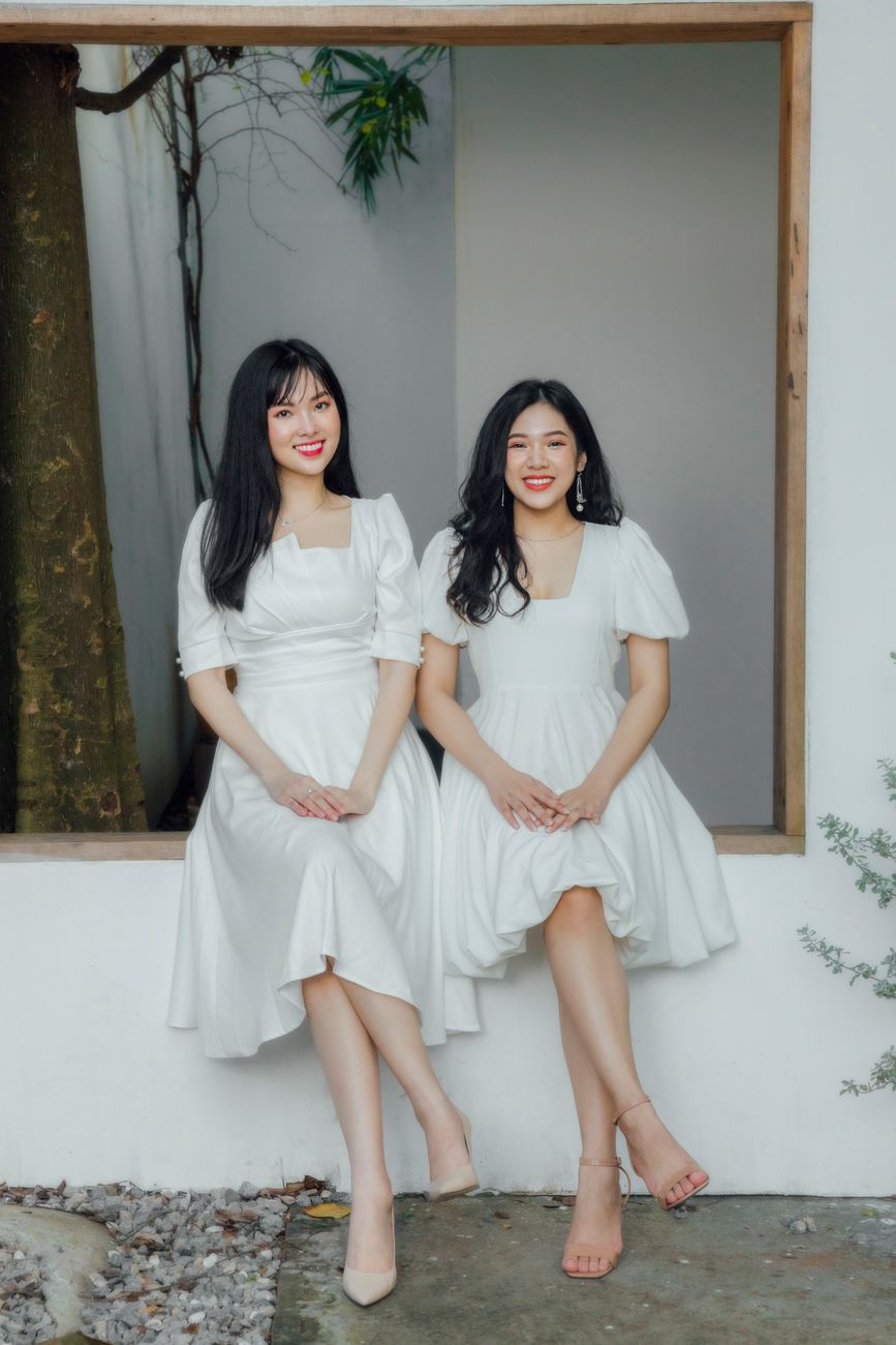 Two women sitting on a windowsill wearing white dresses, showing fashion and friendship.