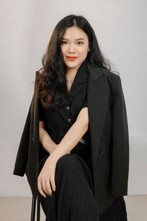 Free Portrait of a smiling Asian woman in black outfit and blazer sitting with crossed legs. Stock Photo