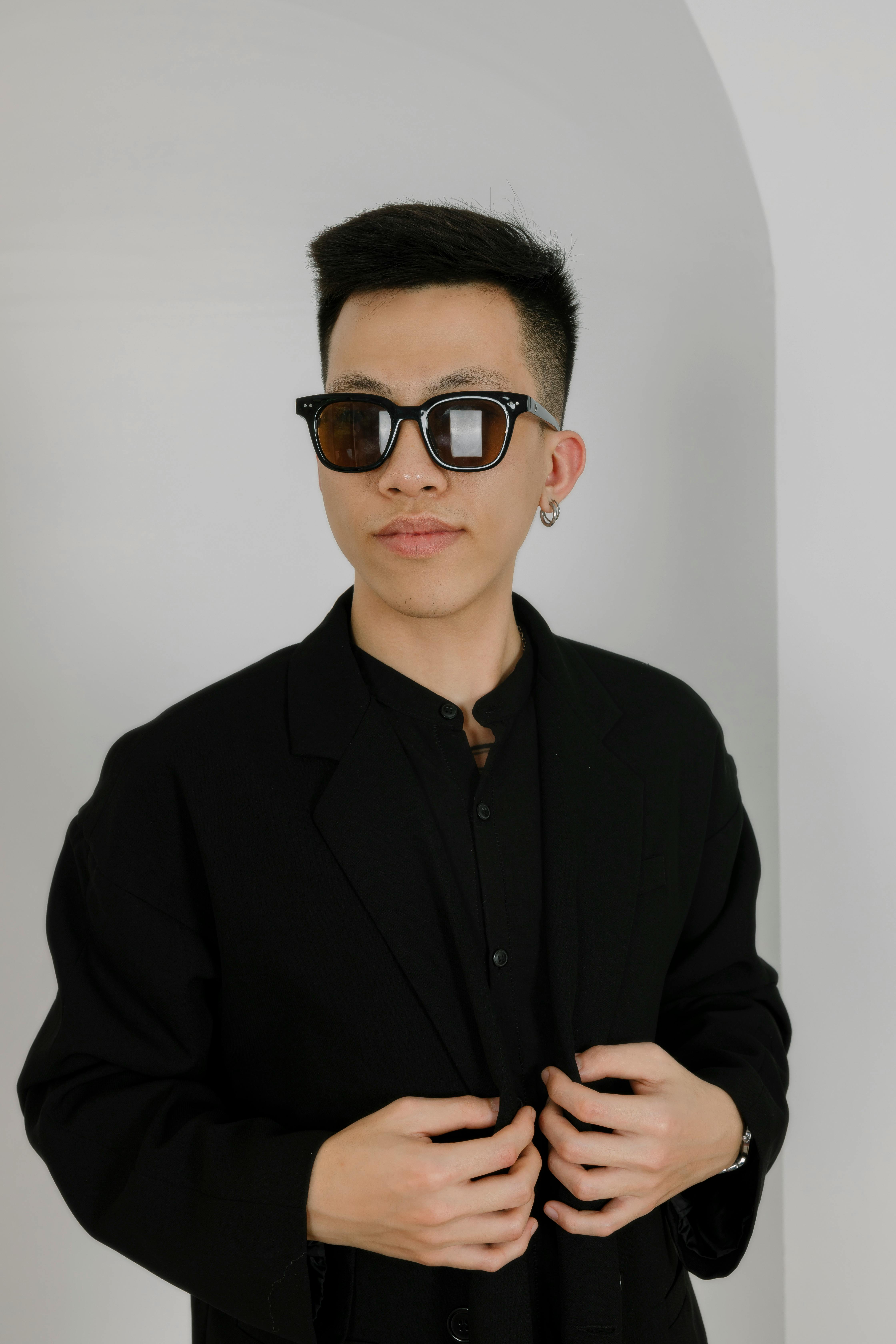 Free Young man wearing sunglasses and a black blazer against a neutral background. Stock Photo