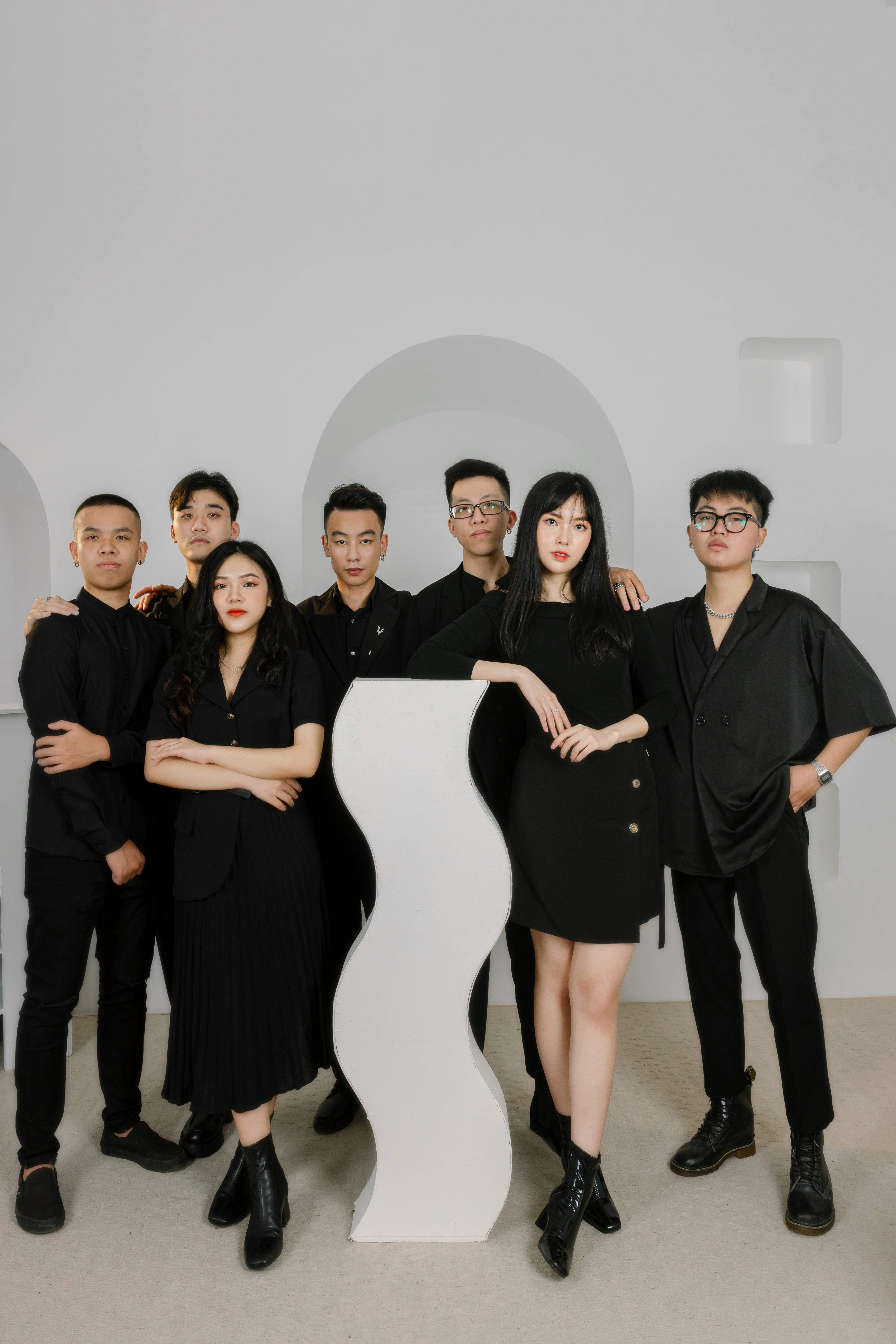 Stylish group portrait with seven friends in black clothing against a minimalist white studio setting.
