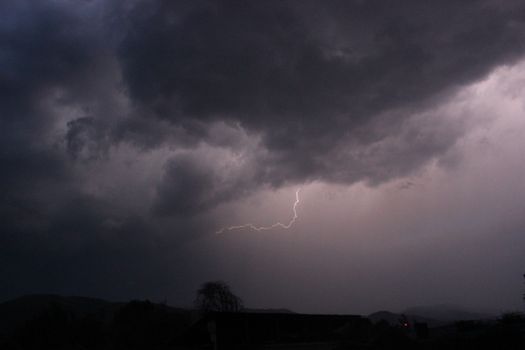 A powerful lightning strike illuminates the dark clouds in a dramatic night sky scene.