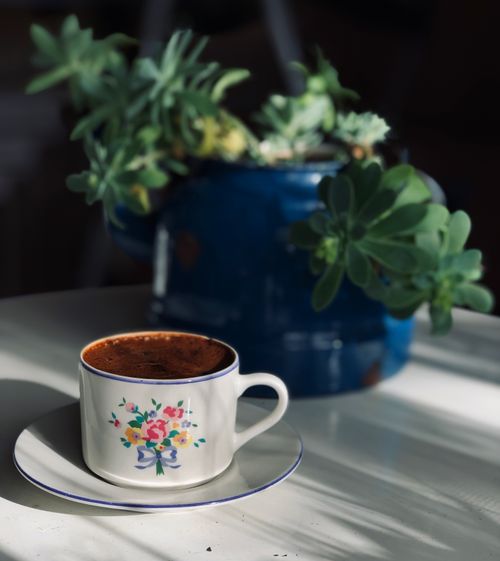 Free A floral ceramic cup of coffee on a saucer next to a blue teapot with succulents. Stock Photo