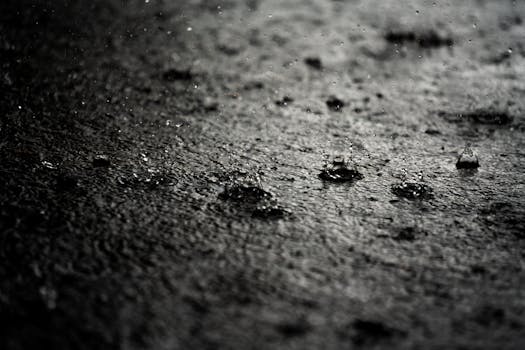 A close-up capture of raindrops splashing on a concrete surface, emphasizing texture and movement.