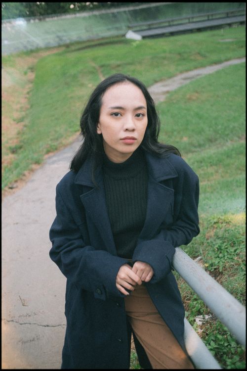 Free A woman stands outdoors in a blue coat, leaning on a railing with a serene expression. Stock Photo