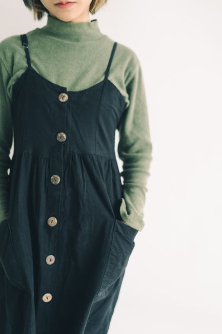 A close-up of a stylish outfit featuring a green turtleneck under a buttoned black dress.