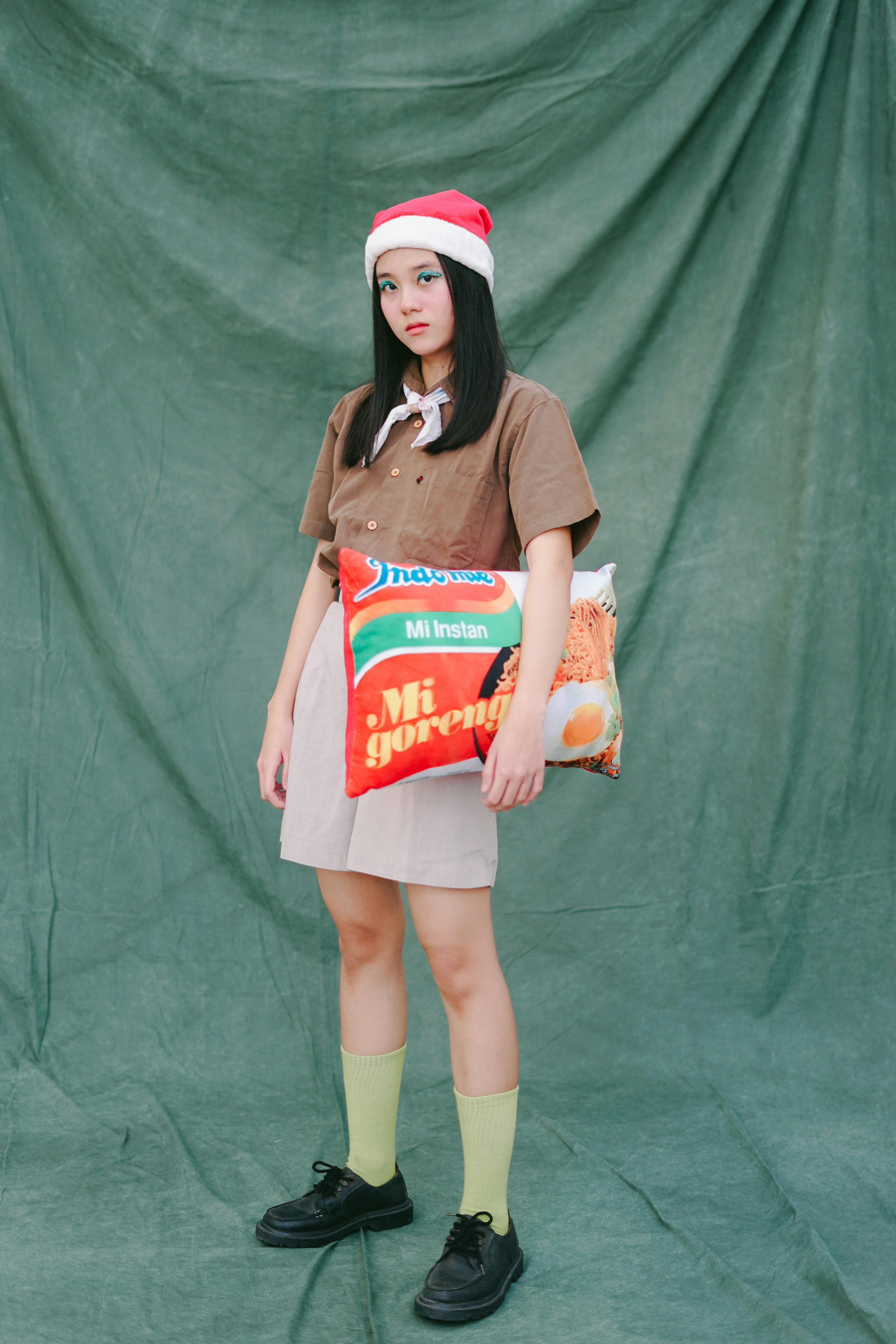 A young woman wearing a Santa hat holds a fun pillow with Indo-food packaging design.